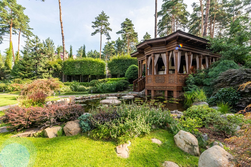 Stunning Alpharetta curb appeal with vibrant landscaping, manicured lawn stripes, lush plants, stone paths, and elegant wooden gazebo under sunny skies