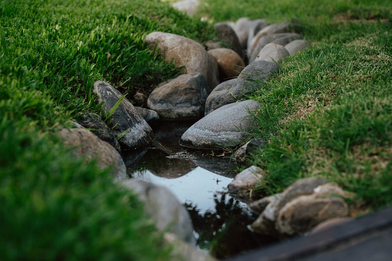 Rock-lined lawn drainage channel improving water flow in an Alpharetta lawn after rainfall.